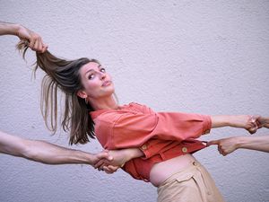 Een foto van een lachende danseres van het Danscollectief Arnhemse Meisjes die aan meerdere kanten wordt vastgepakt door allemaal handen en armen
